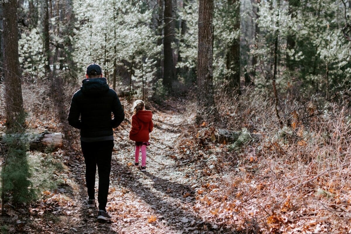 An adult and a child walking in a forest.